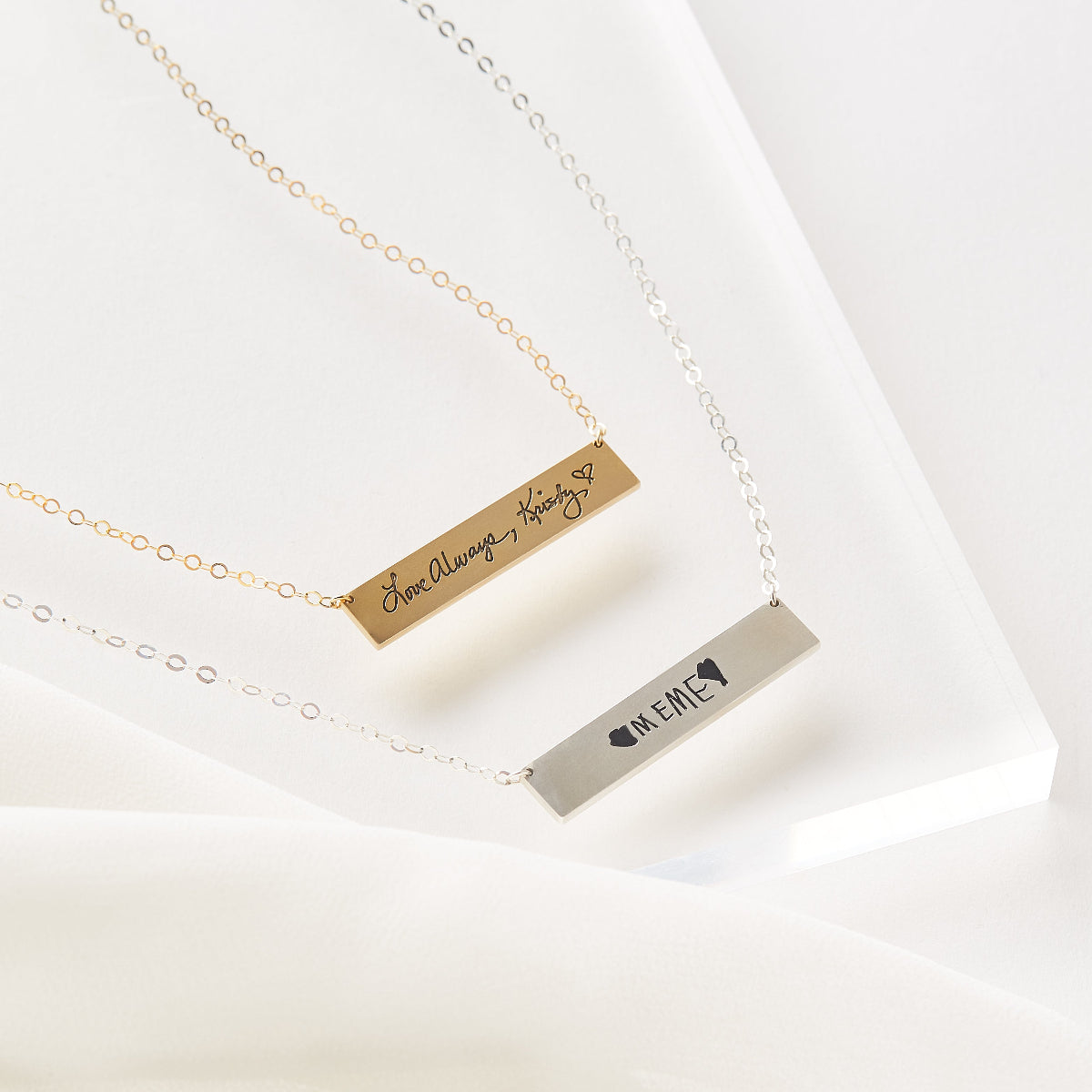 Two gold and silver bar necklaces with engraved text on a white background