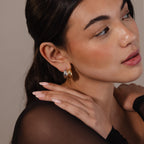Woman with natural makeup and minimal jewelry wears Mixed Metal Puff Studs, touches her shoulder, and gazes slightly to the side.
