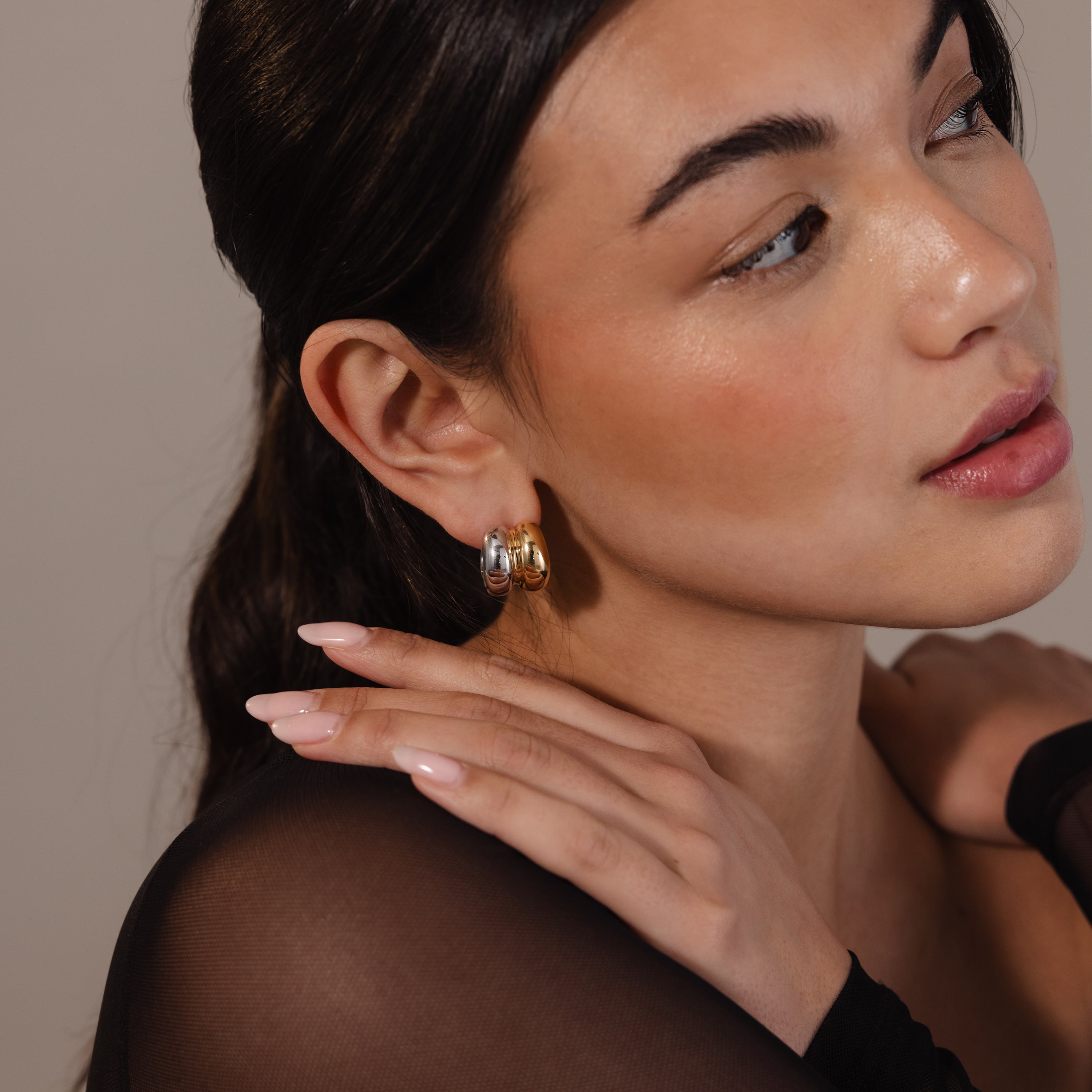 Woman with natural makeup and minimal jewelry wears Mixed Metal Puff Studs, touches her shoulder, and gazes slightly to the side.