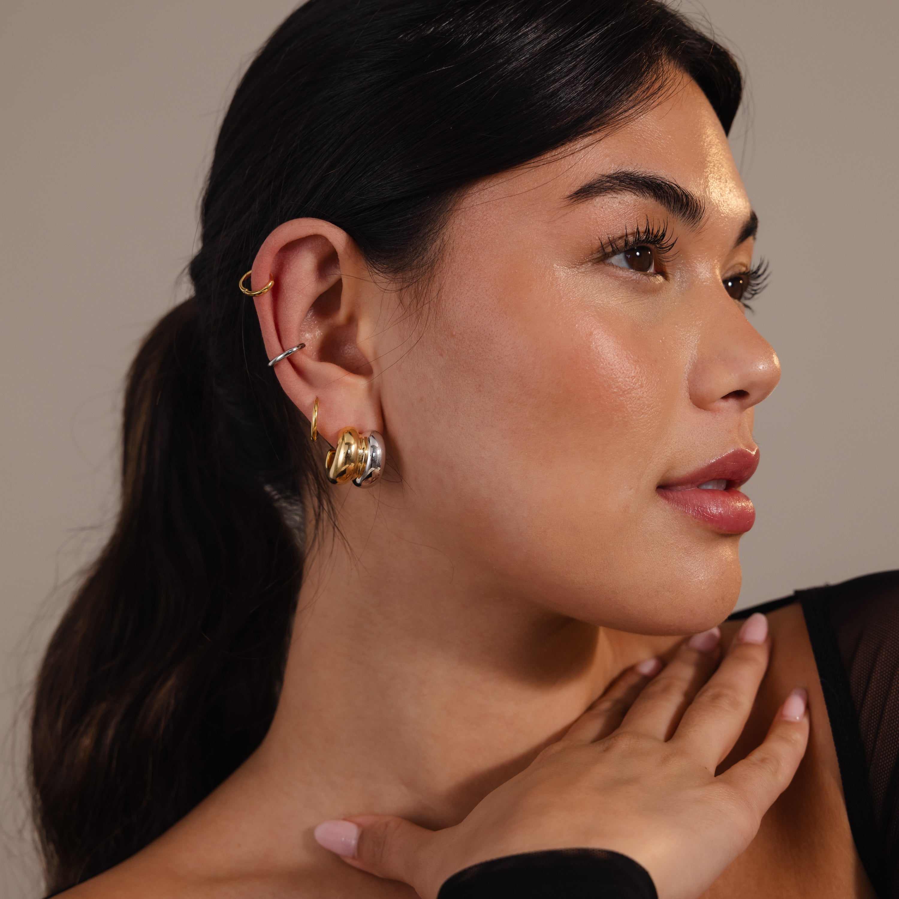 A woman with long dark hair wears minimal jewelry, including the Mixed Metal Puff Studs, as she touches her neck and looks to the side.