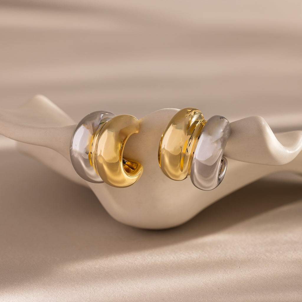 The Mixed Metal Puff Studs set features two pairs of chunky, modern earrings in gold and silver, displayed on a wavy ceramic holder—ideal for minimal jewelry lovers.
