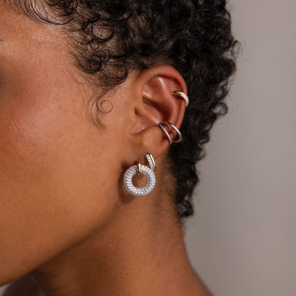Close-up of an ear styled with gold and silver earrings: the featured Half Pave Huggies, a large circular diamond hoop, and two smaller CZ diamond hoops above.