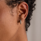 A close-up of a person’s ear wearing a small, textured gold hoop earring, similar to the Half Pave Huggies in 18K Gold.