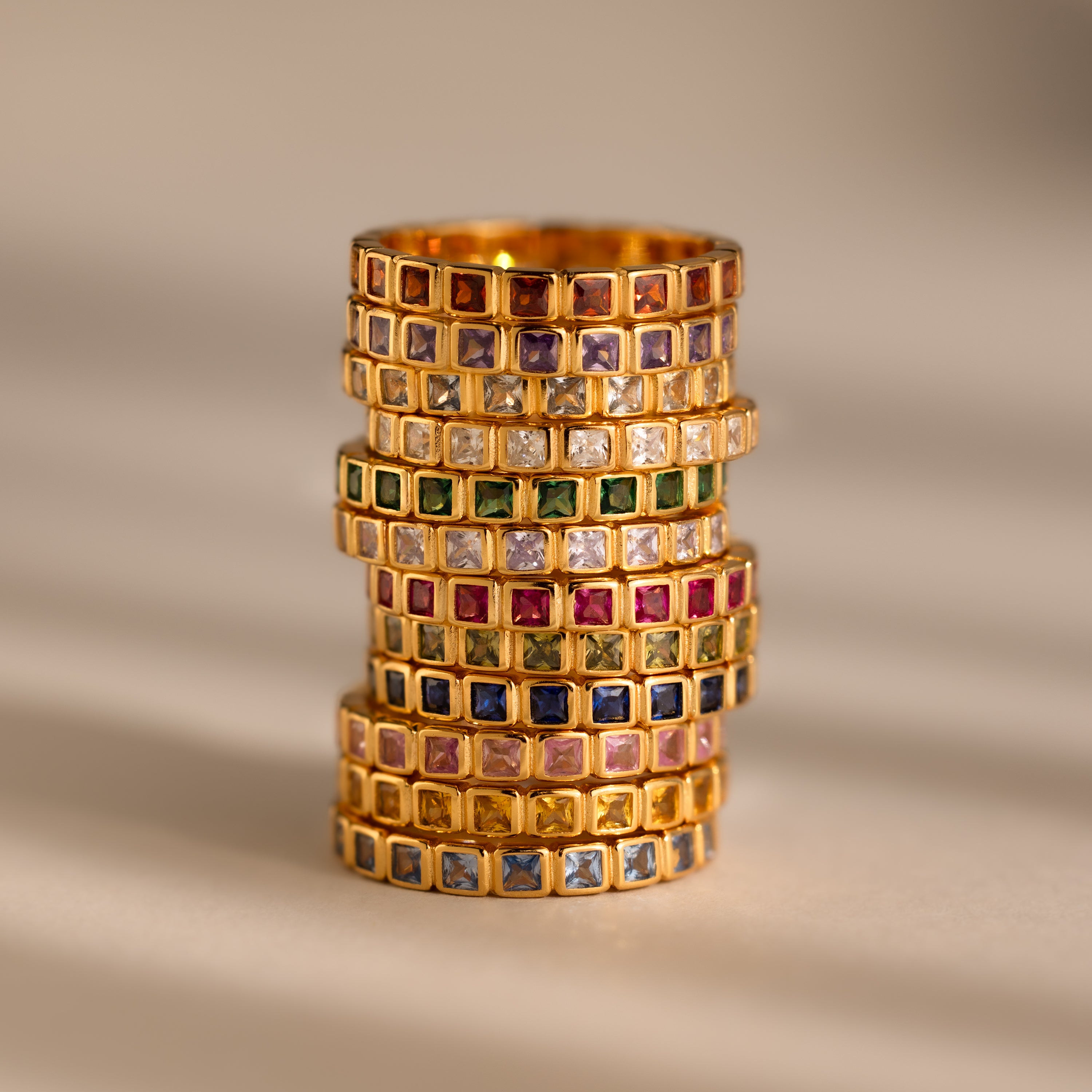 The Eternity Bezel Alexandrite Ring features gold with square-cut alexandrite gemstones set in multiple rows, showcased on a neutral background.