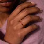 A hand wearing the Eternity Bezel Sapphire Ring, featuring red square-cut gemstones and a gold bezel, rests on a lavender sweater.