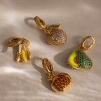 The Emerald Avocado Charm, accented with vibrant pavé stones, brings colorful sparkle to any jewelry collection, beautifully displayed on a beige surface.