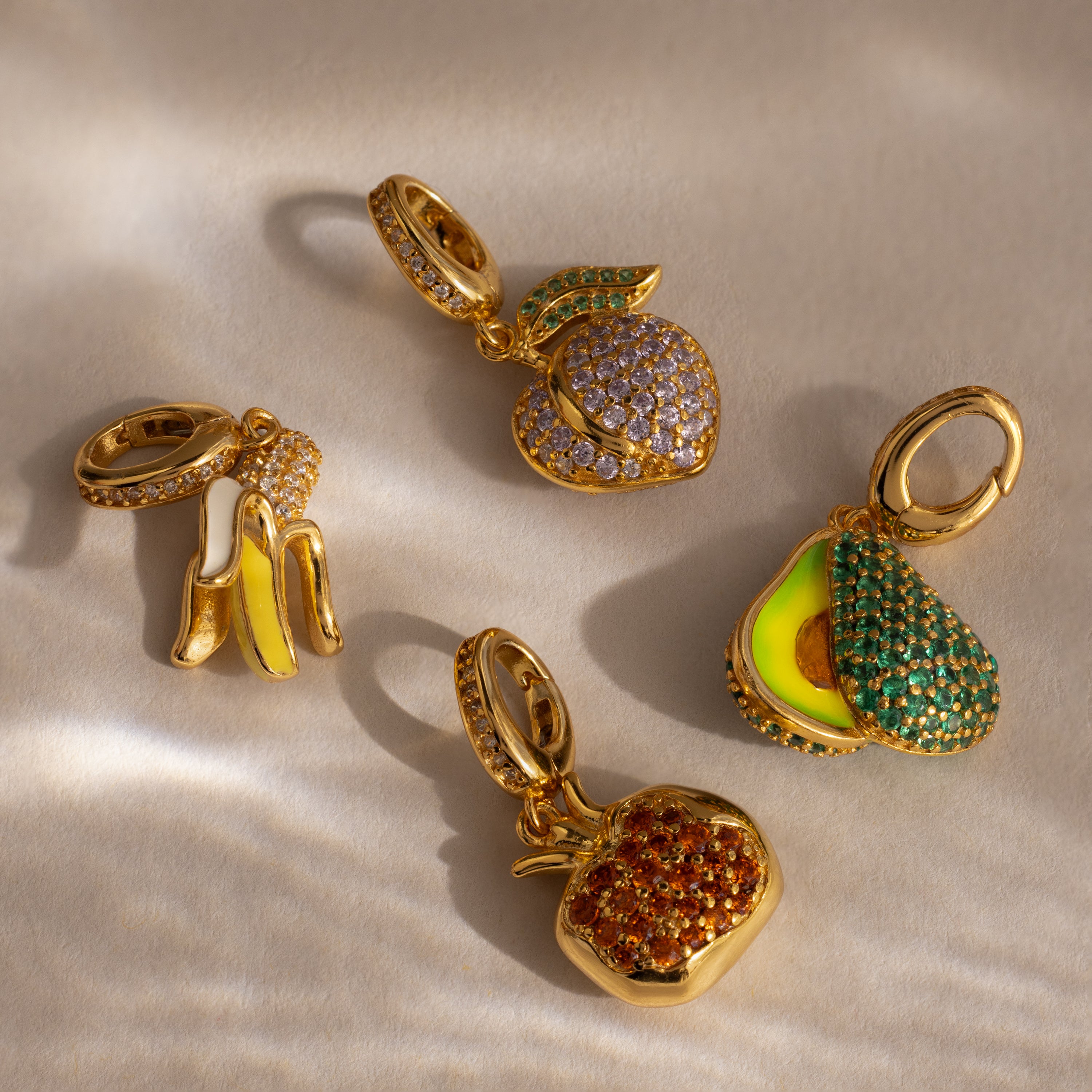 The Emerald Avocado Charm, accented with vibrant pavé stones, brings colorful sparkle to any jewelry collection, beautifully displayed on a beige surface.
