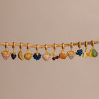 The Amethyst Grape Charm features gold fruit-themed designs with pavé stones, including grapes, cherries, and bananas, hanging from a branch—a stunning addition to any jewelry collection.