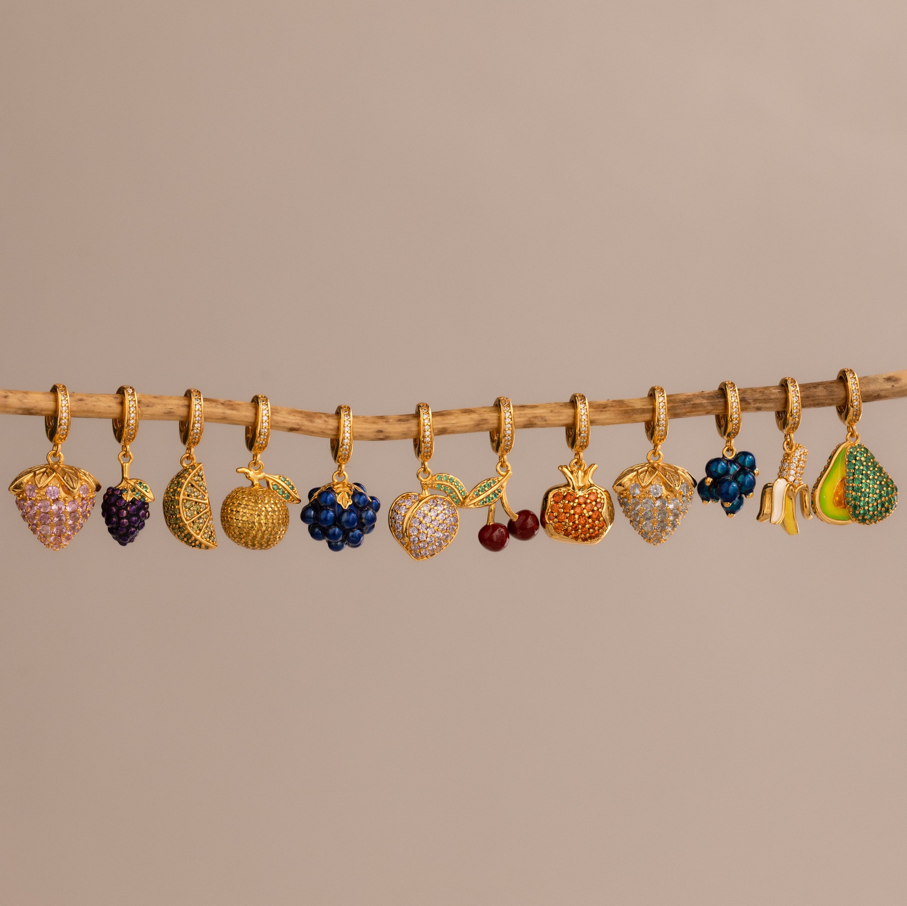 The Topaz Citrus Charm features gold fruit shapes with colorful pavé stones hanging on a branch, bringing vibrant elegance to any jewelry collection.