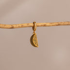 The Peridot Lime Charm features sparkling pavé stones and hangs from a branch against a beige background—a vibrant, eye-catching addition to any jewelry collection.