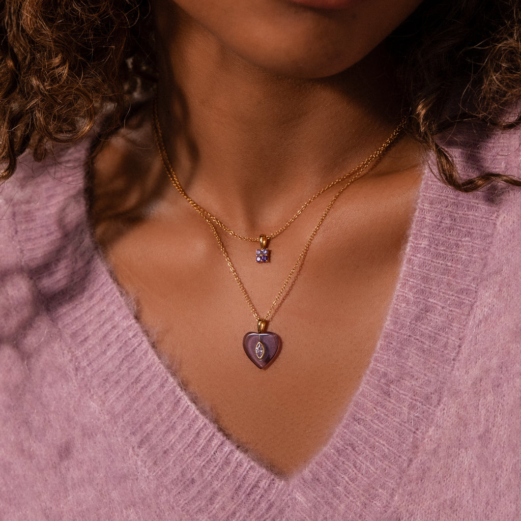 Woman wearing a soft purple sweater and two gold necklaces—one with a heart charm, the other is the Ombre Topaz Flower Necklace featuring a small square pendant.
