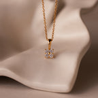 The Ombre Diamond Flower Necklace features a gold chain and a cluster-inspired pendant, displayed on smooth beige fabric.