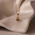 Ombre Peridot Flower Necklace with a gold chain and floral pendant, reminiscent of a Gradient Gemstone Necklace, displayed on a smooth, cream-colored surface.