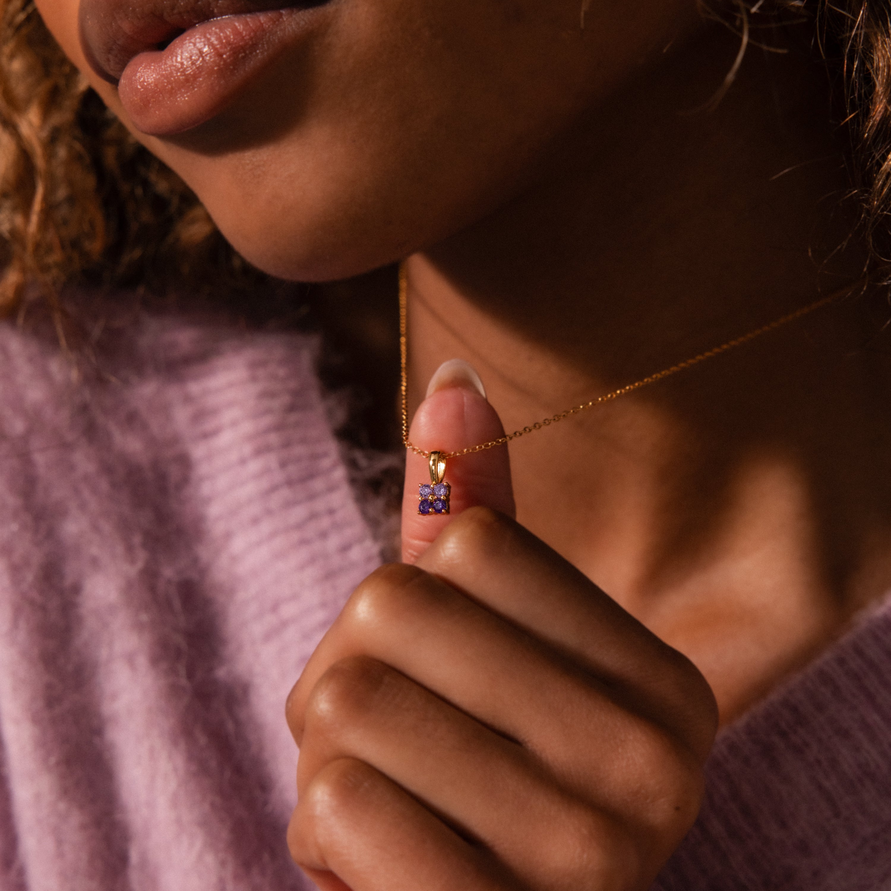 Woman in a purple sweater holding an Ombre Aquamarine Flower Necklace with a small flower-shaped pendant near her neck.