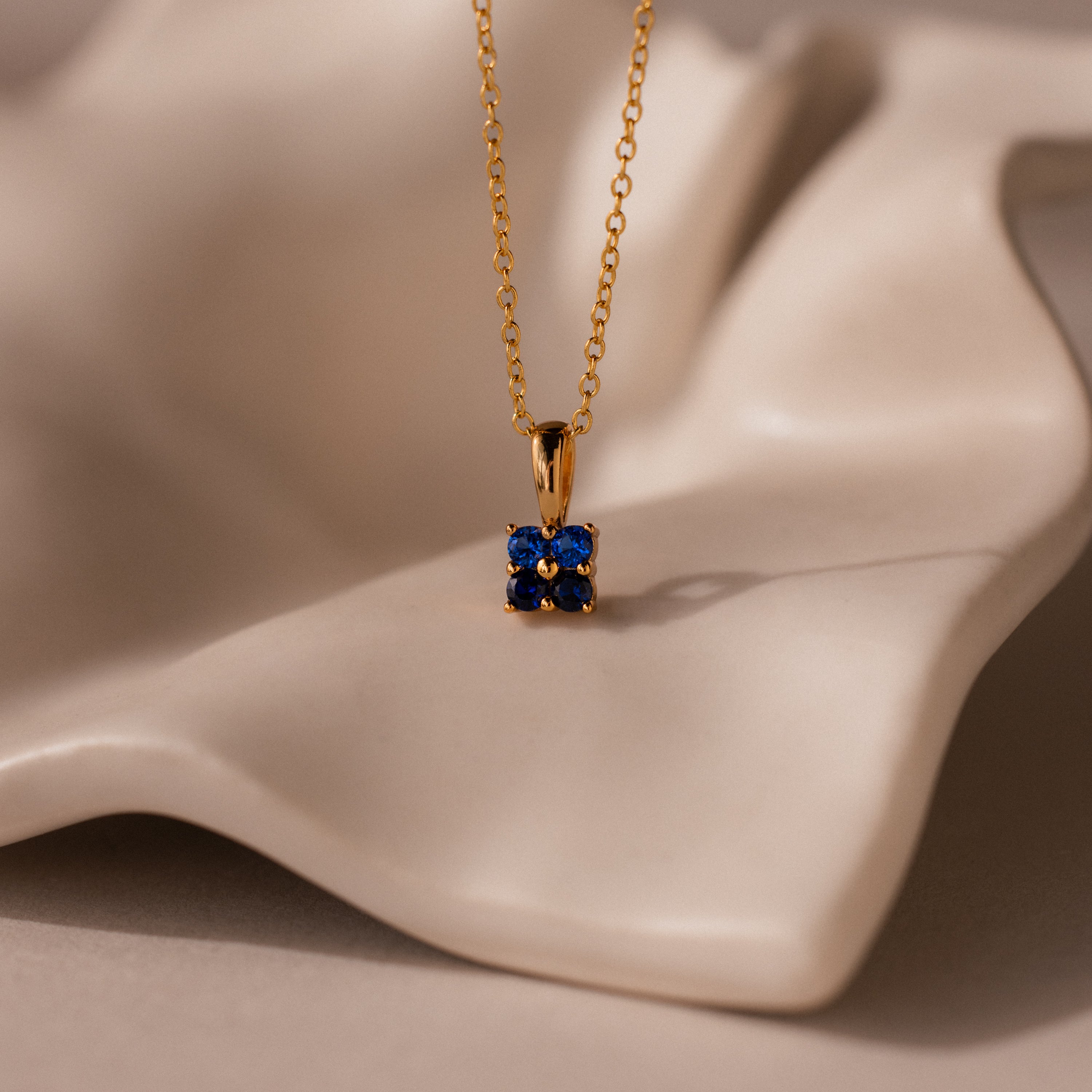 Ombre Sapphire Flower Necklace displayed on a soft, beige, wavy surface.