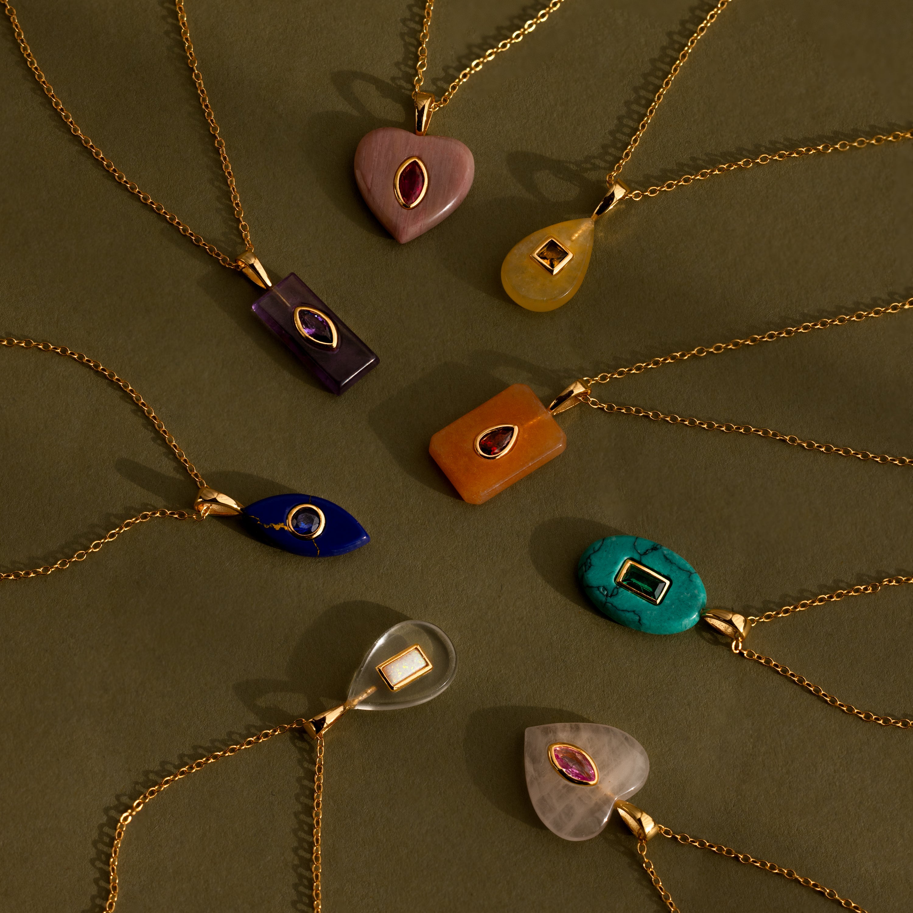 Eight Topaz Crystal Necklaces with bezel-set pendants are displayed in a circular arrangement on an olive surface.