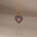 Alexandrite Crystal Necklace: A heart-shaped gold pendant with a central gem, elegantly hanging from a gold chain and showcased on a soft beige background. Perfect as birthstone jewelry or a stunning Birthstone Crystal Necklace for any occasion.