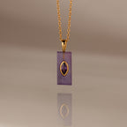 Gold chain necklace with a rectangular purple pendant and gold accent, reflected on a smooth surface—an elegant Amethyst Crystal Necklace perfect for adding a touch of birthstone jewelry to any look.