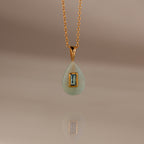 Aquamarine Crystal Necklace: Features a gold chain with a teardrop-shaped green birthstone pendant accented by a rectangular blue gemstone at the center—an eye-catching piece of jewelry.