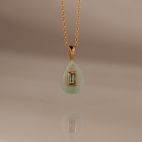 Aquamarine Crystal Necklace: Features a gold chain with a teardrop-shaped green birthstone pendant accented by a rectangular blue gemstone at the center—an eye-catching piece of jewelry.