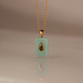 The Peridot Crystal Necklace features a rectangular green crystal pendant in a gold bezel setting, highlighted by a gold-trimmed teardrop accent at the center.