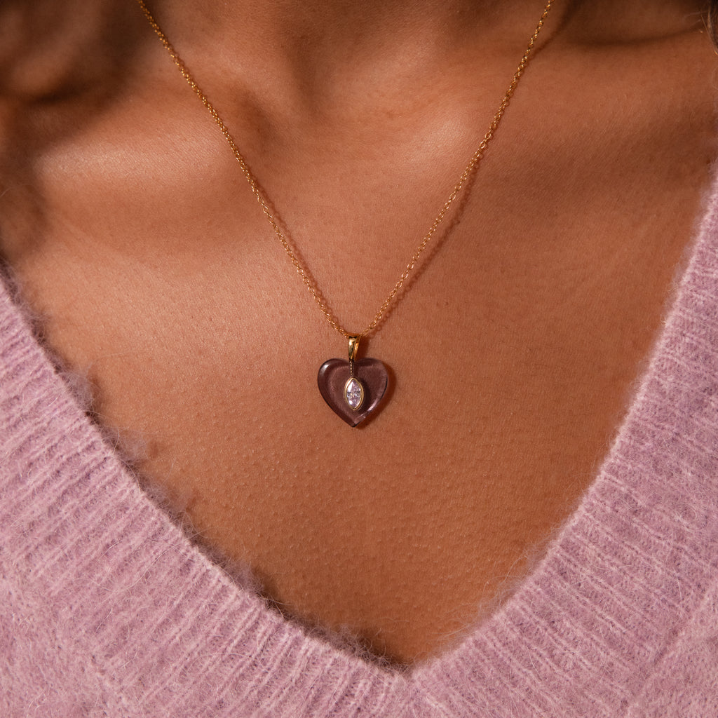 The Aquamarine Crystal Necklace, with its heart-shaped pendant, adds a charming touch to any look when styled over a pink fuzzy V-neck sweater.