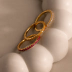 The Endless Eternity Birthstone Ring, along with two other gold gemstone rings, rests on a smooth, white, rounded surface.