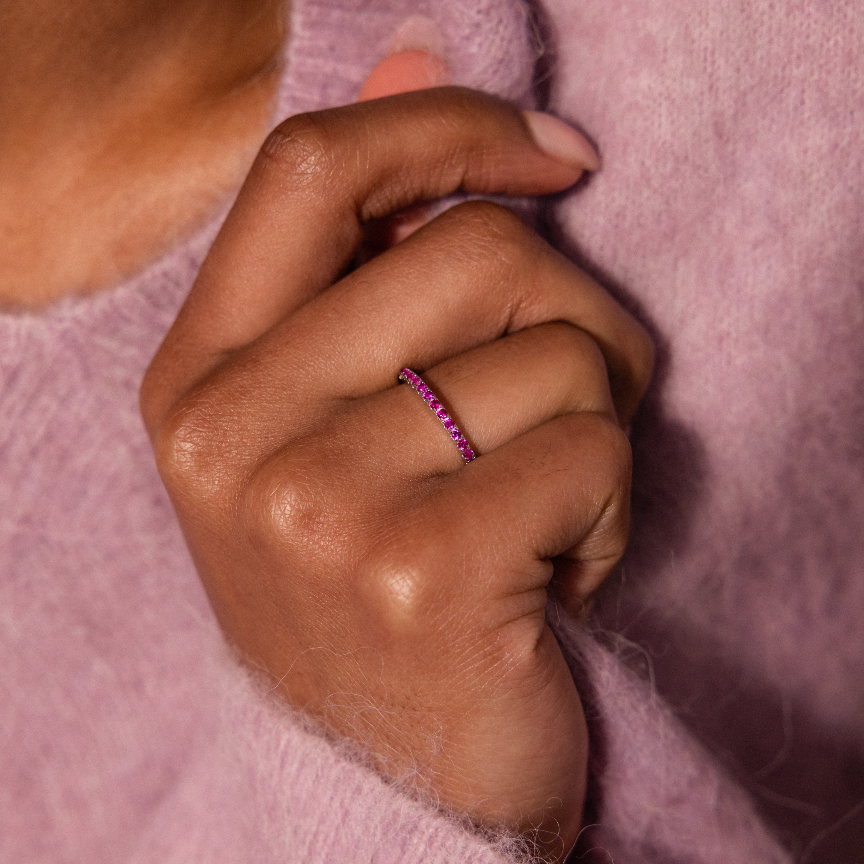 A hand wearing the Lace Eternity Garnet Ring, with a mauve fuzzy sweater in the background.
