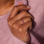 A hand adorned with the Endless Eternity Ruby Ring, featuring elegant pink gemstones, with a fuzzy pink sweater in the background.