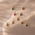Nine Square Bezel Diamond Charms with gold frames are displayed on a beige textured surface under soft light—a stunning showcase of gemstone jewelry.