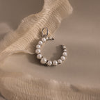 The Pearl Moon Charm, a crescent-shaped pearl earring inspired by celestial beauty, is displayed on soft cream-colored fabric.