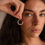 A woman with long dark hair holds up the Pearl Moon Charm in 18K Gold near her face, highlighting the celestial elegance of this unique pearl jewelry piece.