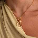 The Pearl Moon Charm in White Gold shines elegantly against draped beige fabric, featuring a celestial design perfect for layering with your favorite gemstone pendants.
