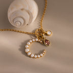 The Pearl Moon Charm necklace features celestial-inspired gemstone and pearl charms, beautifully displayed next to a white seashell on beige.