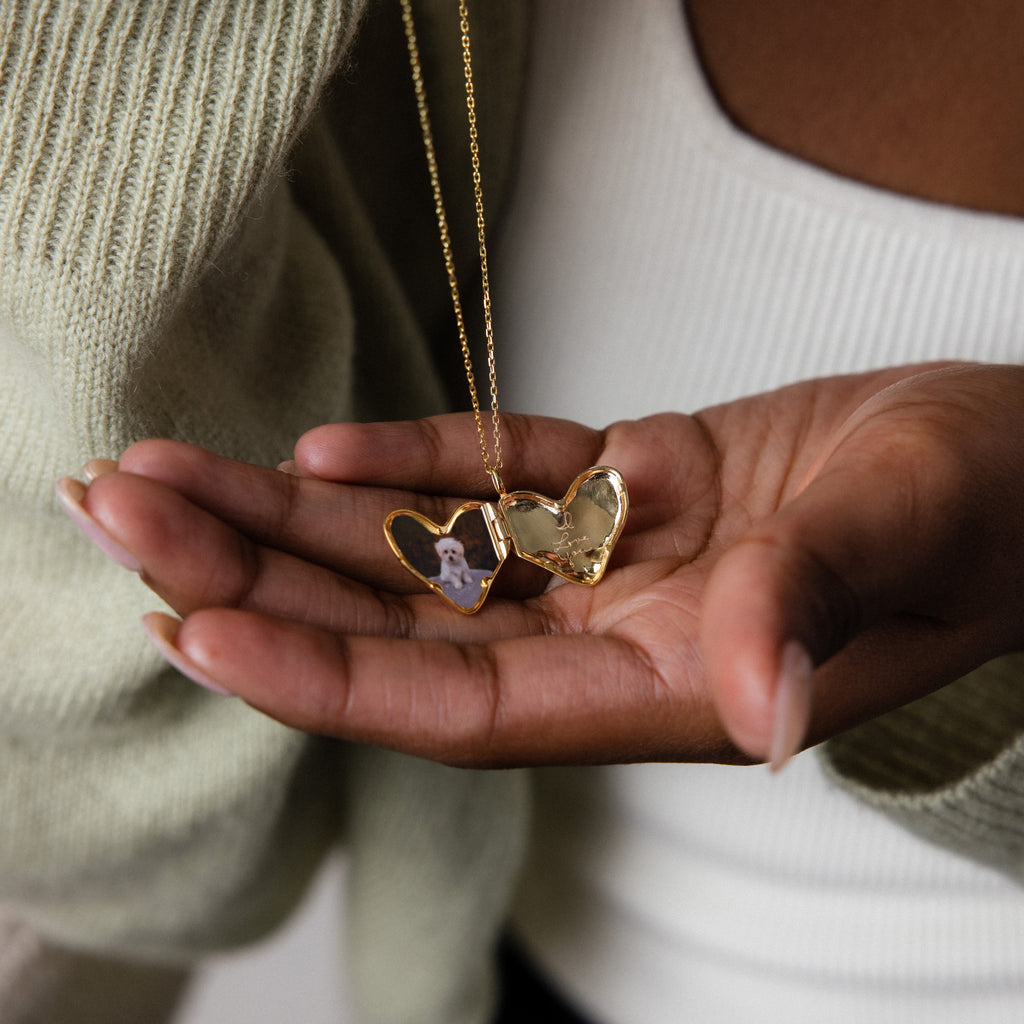 A hand holds the Organic Heart Locket Necklace, open to reveal a tiny photo on one side and an empty space on the other—ideal as keepsake jewelry or for adding a personal engraving.