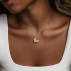 A woman wearing the Organic Heart Locket Necklace in 18K Gold and a white square-neck top, showcasing elegant keepsake jewelry.