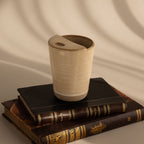 The Everyday Ceramic Mug in beige with a speckled glaze sits atop stacked vintage books, soft shadows behind.