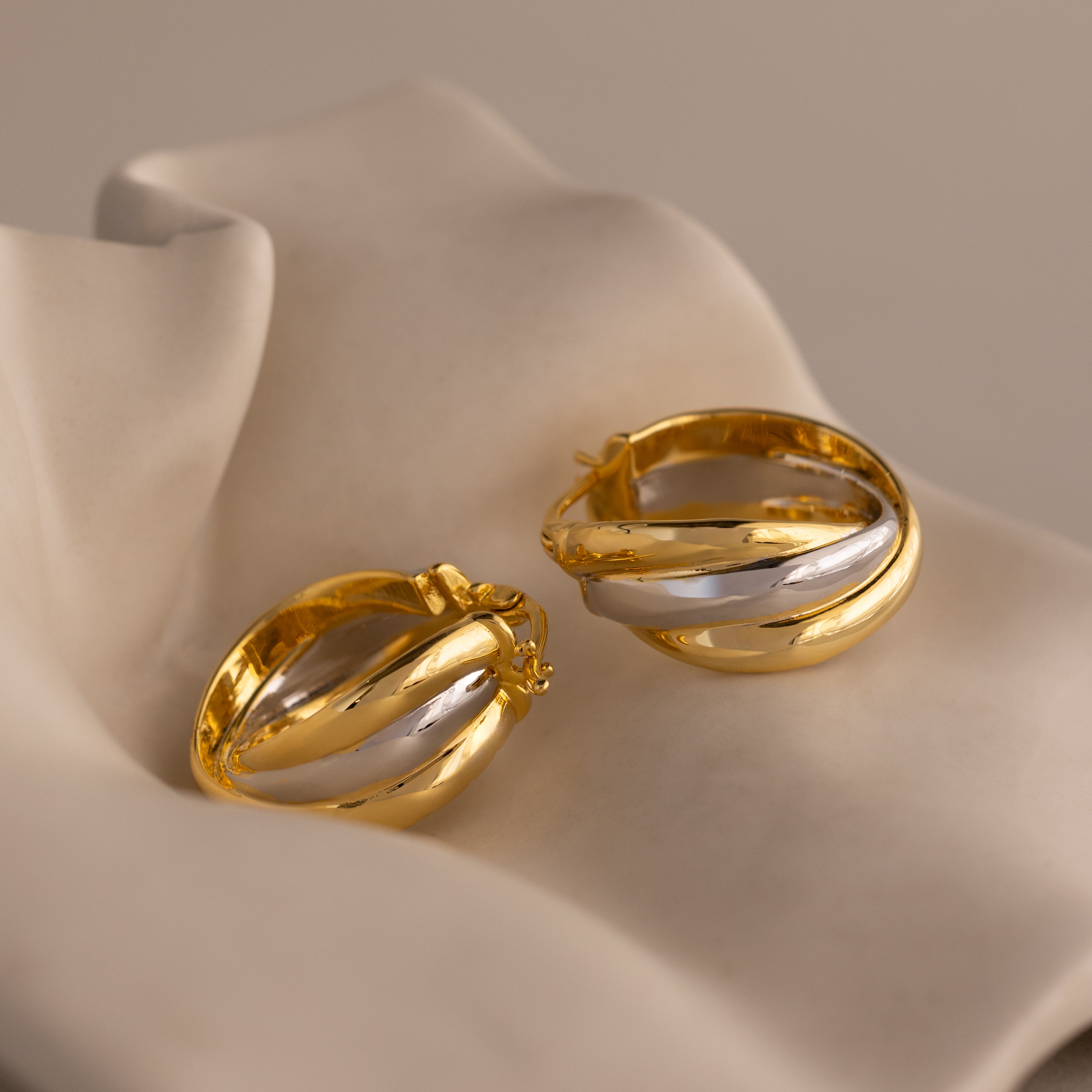 Intertwined Mixed Metal Hoops showcased on a soft, light-colored fabric background.
