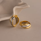 The Intertwined Mixed Metal Hoops, shown in gold and silver beside a white ceramic dish on a neutral background, bring effortless style and modern flair to any outfit.
