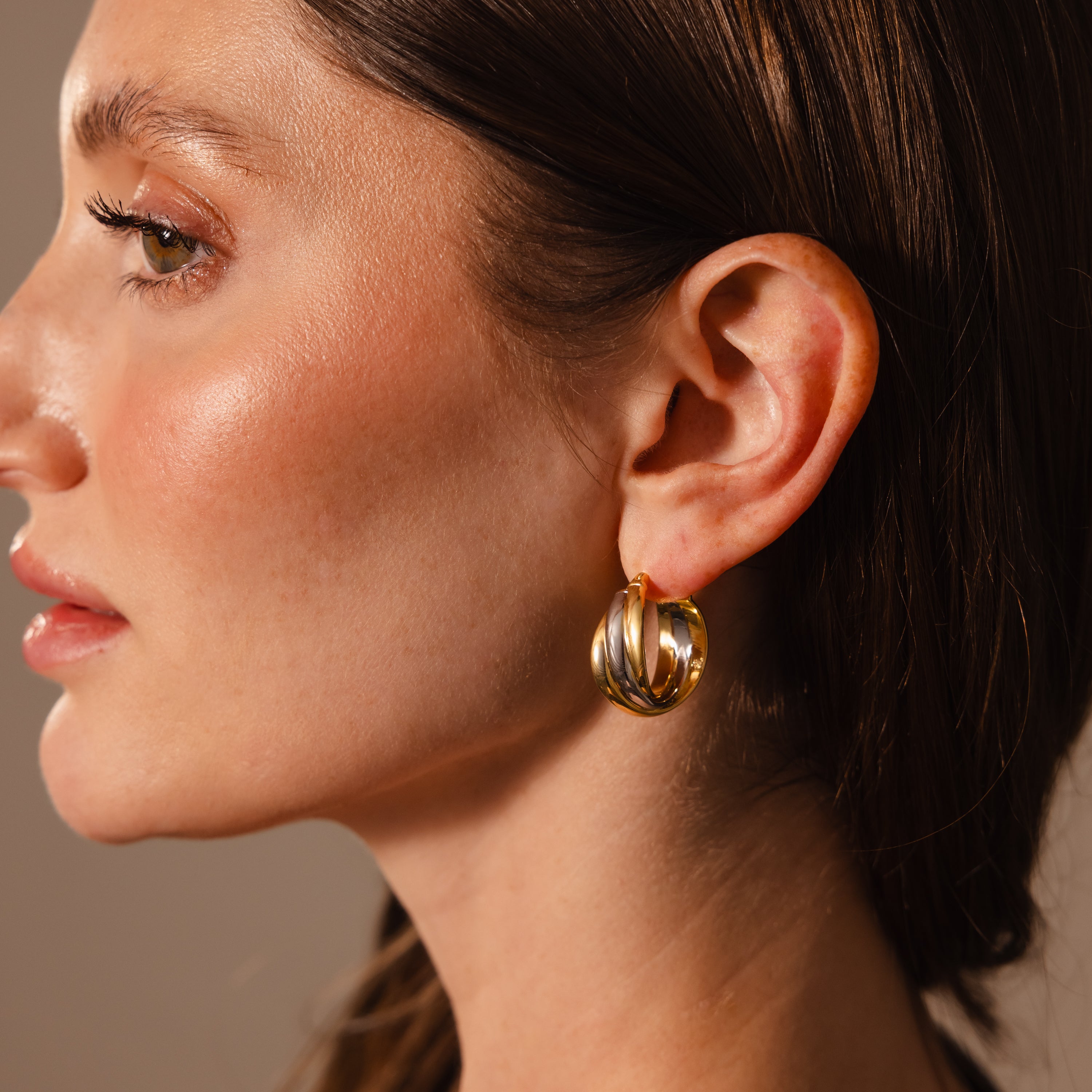 A woman with smooth skin is shown in profile wearing Intertwined Mixed Metal Hoops against a neutral background.