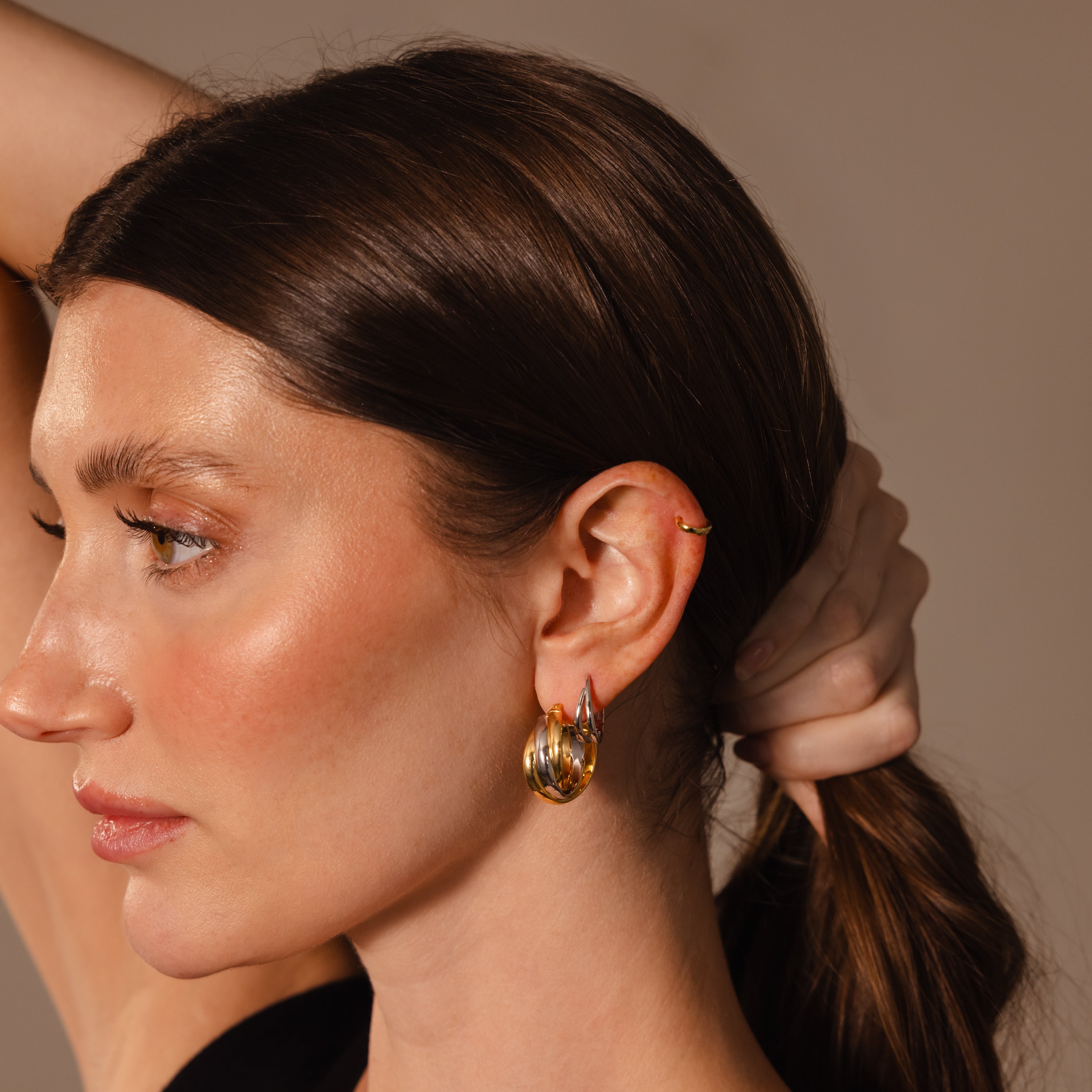 Woman with brown hair in a ponytail wears Intertwined Mixed Metal Hoops—gold and silver earrings—alongside a small gold ear cuff, shown in side profile.
