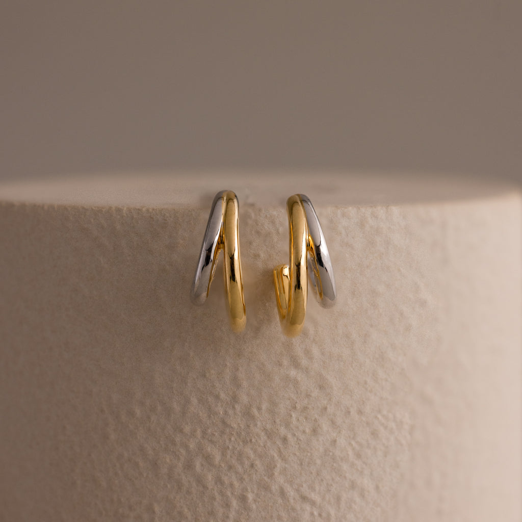 The Mixed Metal Duo Hoops, stylish gold and silver earrings, are displayed on a textured, light-colored surface.