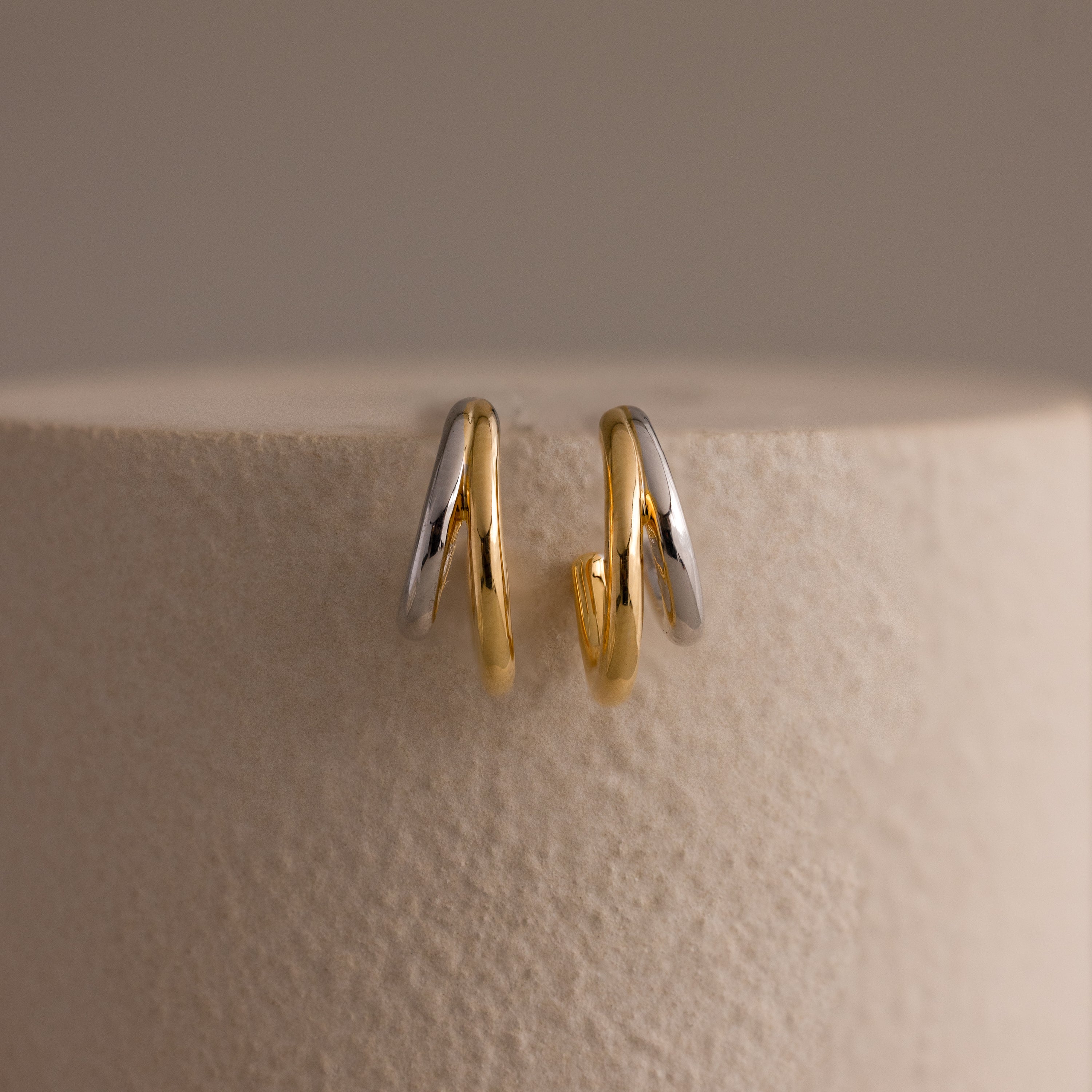 The Mixed Metal Duo Hoops, stylish gold and silver earrings, are displayed on a textured, light-colored surface.