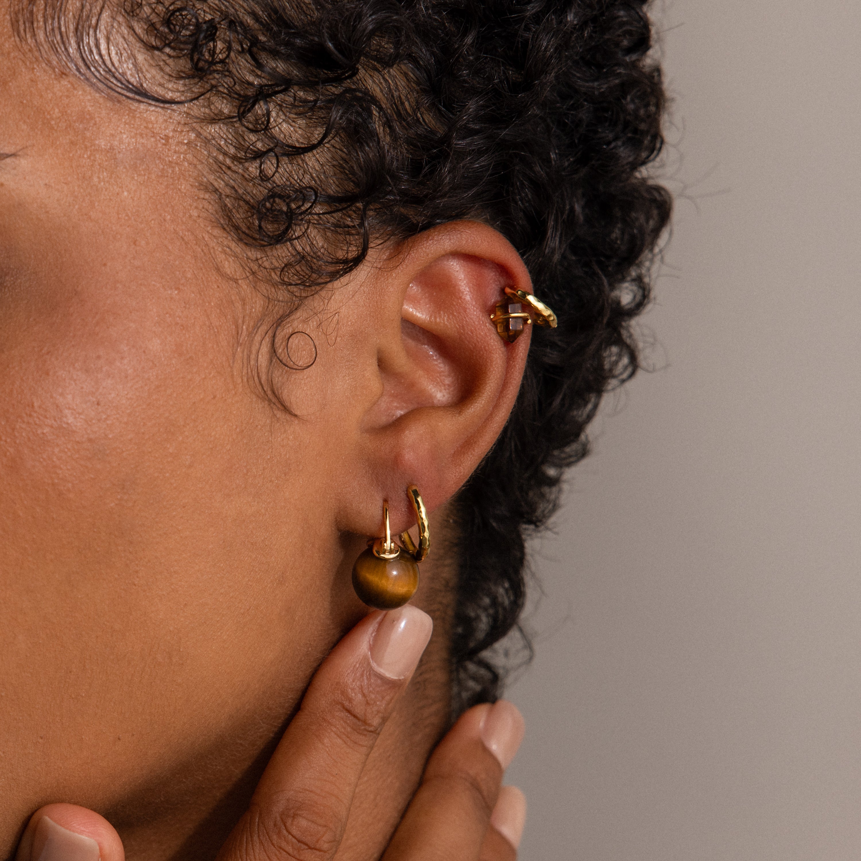 Close-up of an ear wearing Tiger's Eye Dome Drop Earrings, with a hand gently touching the earlobe.