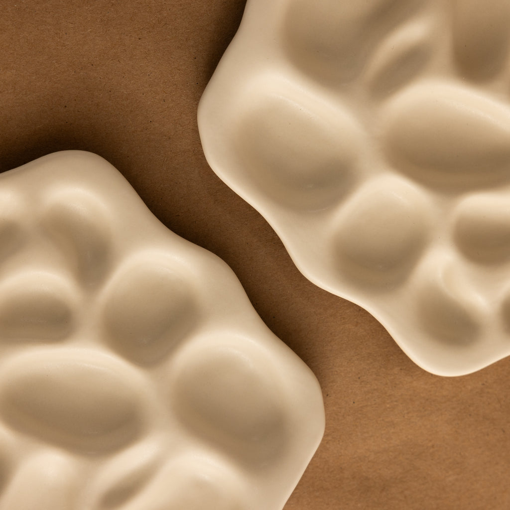 The Mini Organic Treasure Trove Jewelry Dish features two wavy, cream-colored ceramic dishes with unique shapes, ideal for holding keepsakes or jewelry on any surface.