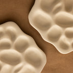 The Mini Organic Treasure Trove Jewelry Dish features two wavy, cream-colored ceramic dishes with unique shapes, ideal for holding keepsakes or jewelry on any surface.