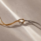 The Love Knot Chain Necklace in Mixed Metal features intertwined gold and silver snake chains tied in a knot, showcased on a neutral background with soft lighting.