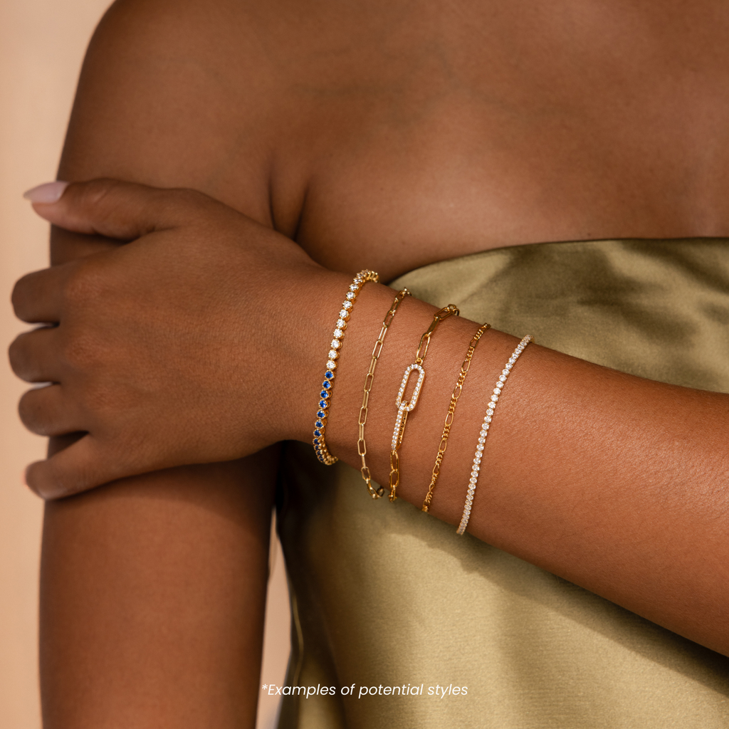 A person in a gold satin dress wears four Mystery Jewelry gold and beaded bracelets, each piece adding unique flair and whimsical charm to their elegant ensemble.
