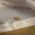 Gold geometric flat back blue topaz stud earrings on a textured stone surface