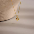The Moonstone Charm Necklace features a gold chain with a small circular pendant, beautifully displayed on a neutral textured background—an elegant piece ideal for moonstone jewelry lovers.